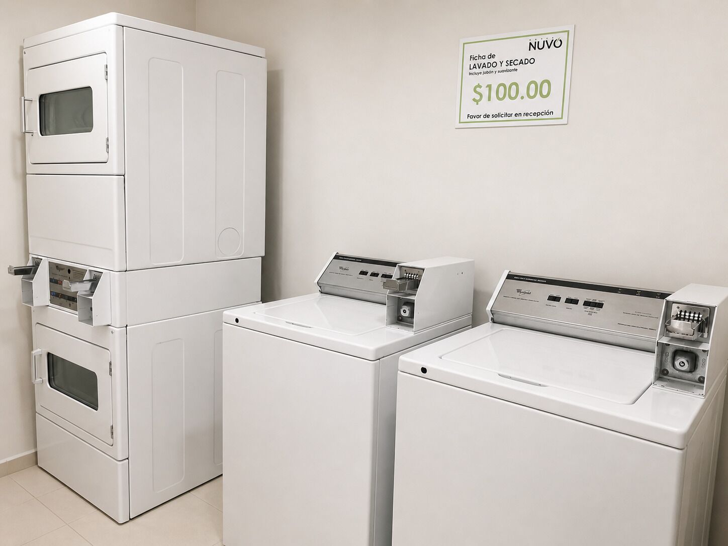 A laundry area with stacked washers and dryers, a sign indicating a $100.00 fee for laundry and dry cleaning, and a note to request in reception.