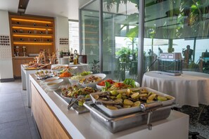 A buffet with various dishes, a coffee station, and a view of the outdoors through large windows. - Noom Hotel Conakry (Conakry)