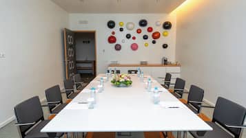 Un salón de conferencias con una larga mesa, sillas, botellas de agua y un centro de mesa floral.