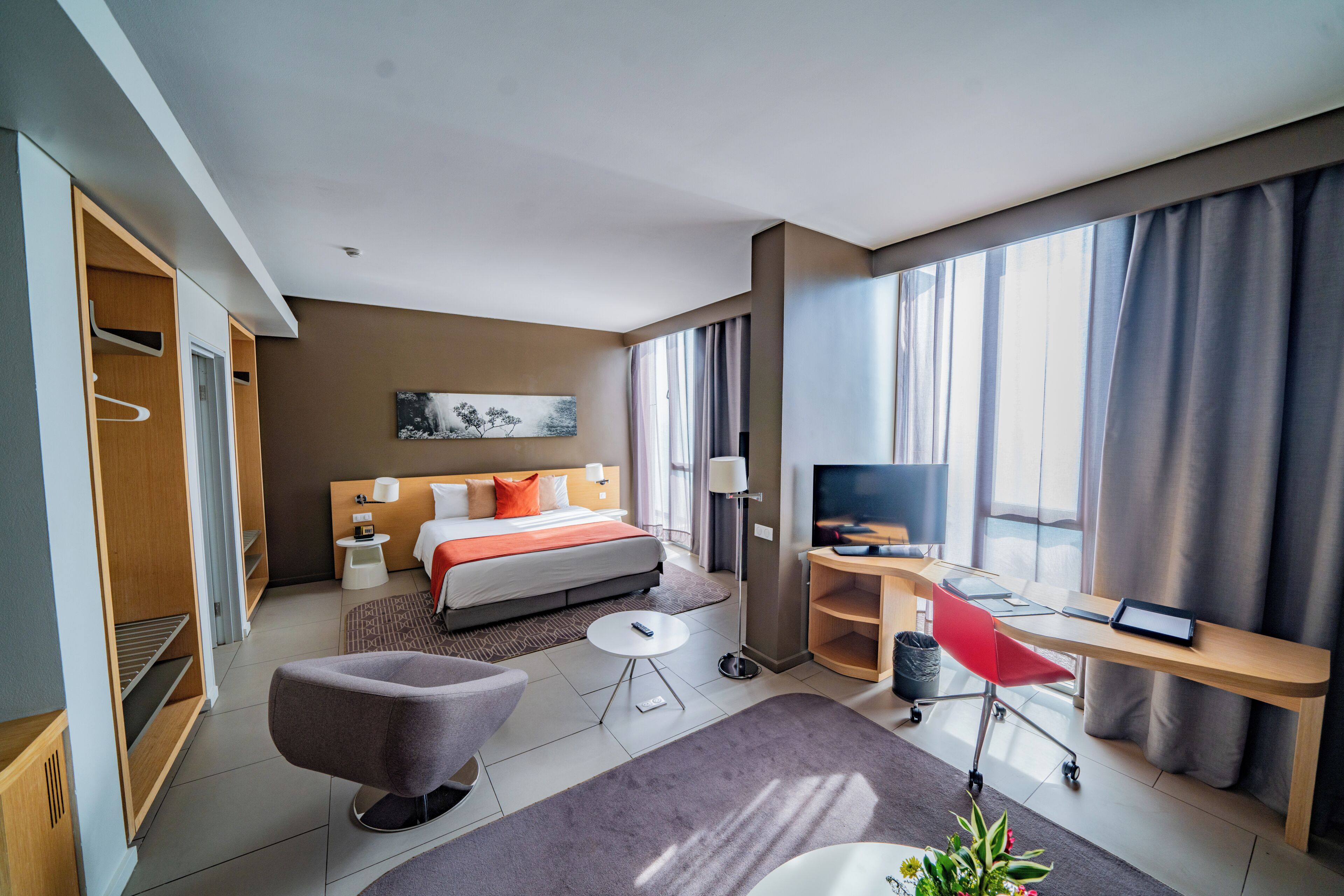 Une chambre d’hôtel comprenant un lit, une table de chevet, une lampe, une télévision, un bureau, une chaise et une petite plante.