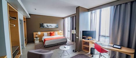 Une chambre d’hôtel comprenant un lit, une table de chevet, une lampe, une télévision, un bureau, une chaise et une petite plante.