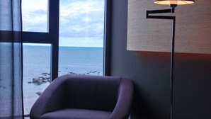 Een moderne kamer met uitzicht op zee, een paarse stoel, een vloerlamp en een klein tafeltje.