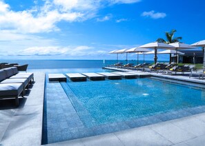 A pool area with lounge chairs and umbrellas, a clear view of the ocean, and a tiled deck. - Noom Hotel Conakry (Conakry)