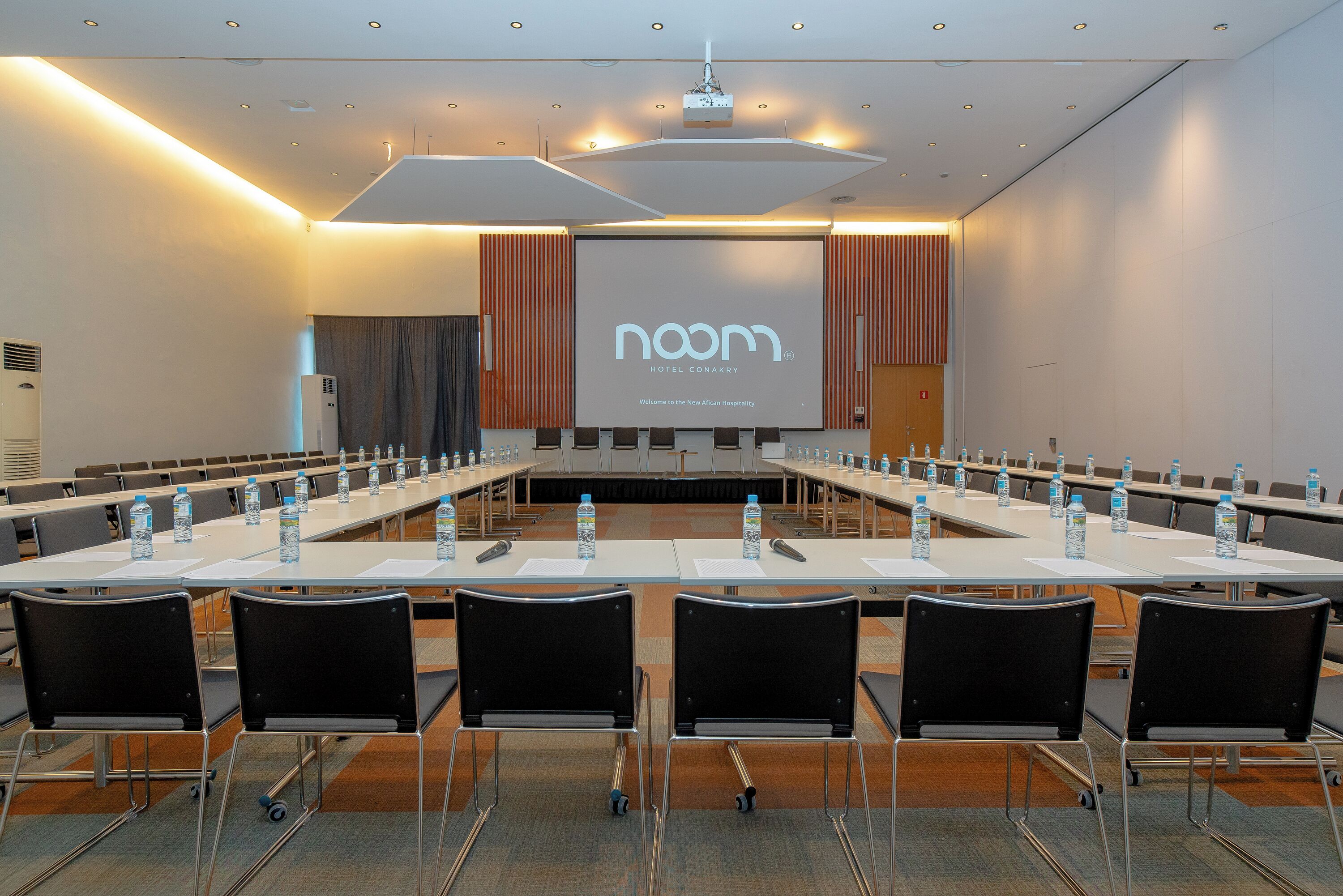 Een vergaderruimte met een lange tafel, stoelen, waterflesjes en een scherm waarop de naam van het hotel staat.