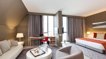 A hotel room with a bed, a desk, a chair, a sofa, a coffee table, and a TV.
