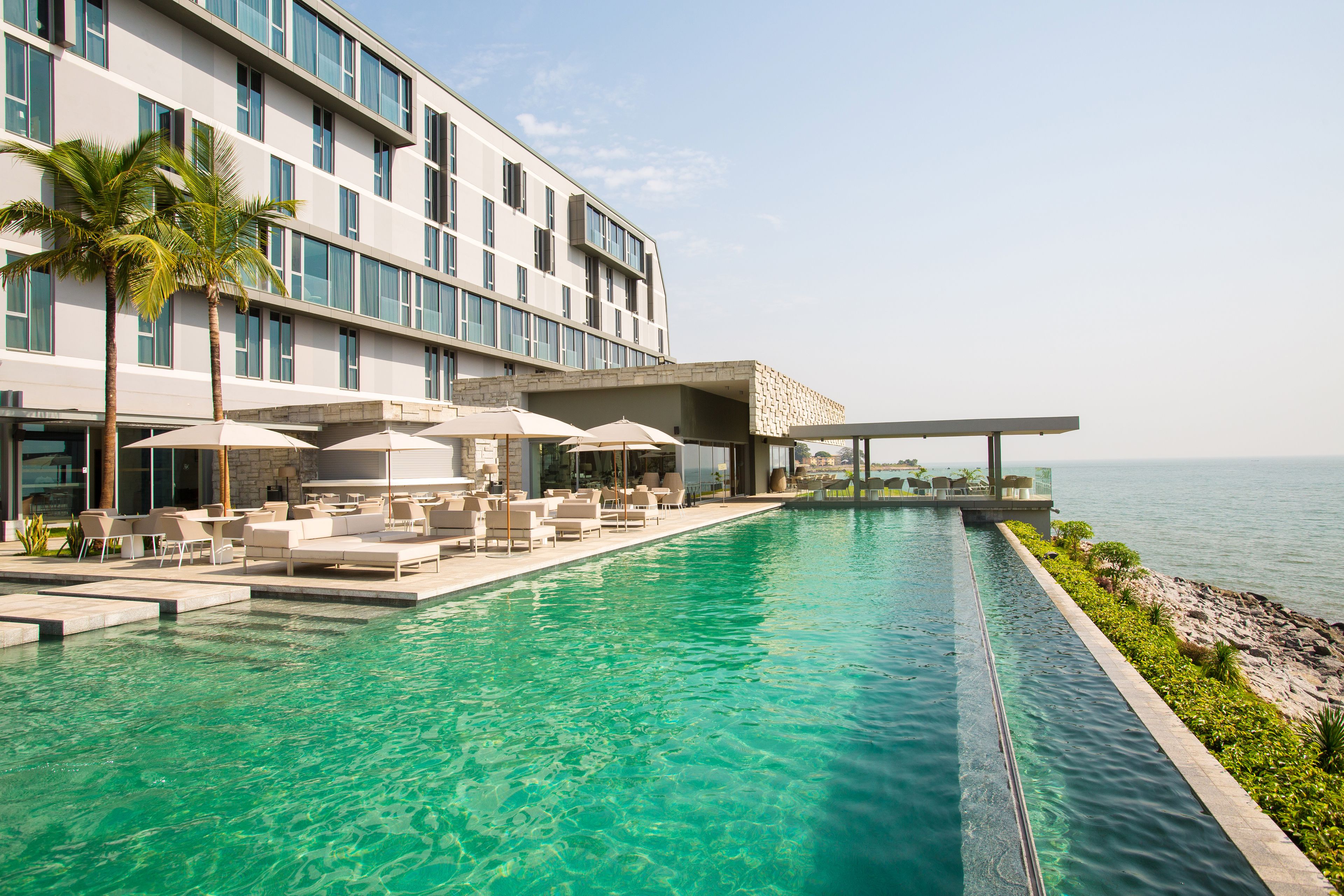 A modern hotel with a pool, outdoor seating, and a view of the sea.