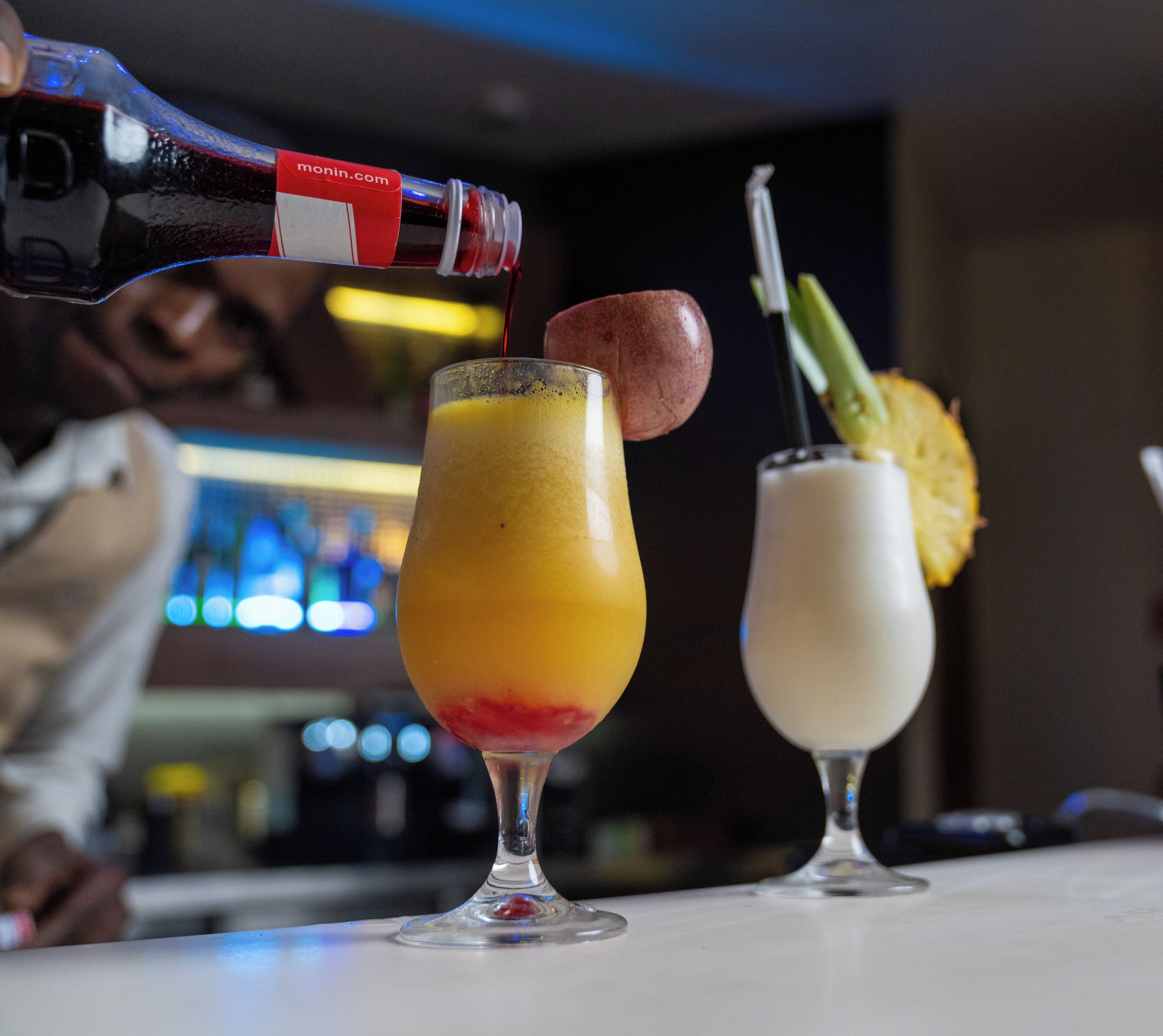 A bar setting with two drinks, one with a fruit garnish and another with a straw.