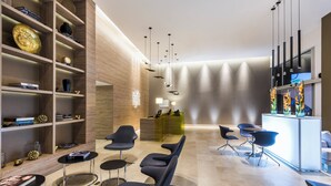 A modern lobby with a reception desk, seating area, and a bookshelf with decorative items. - Holiday Inn Cucuta by IHG (San José de Cúcuta)