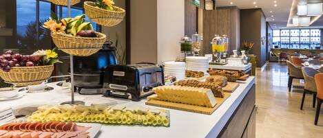 A buffet with various food items, including fruits, cheeses, and meats, arranged on a counter in a modern hotel setting.