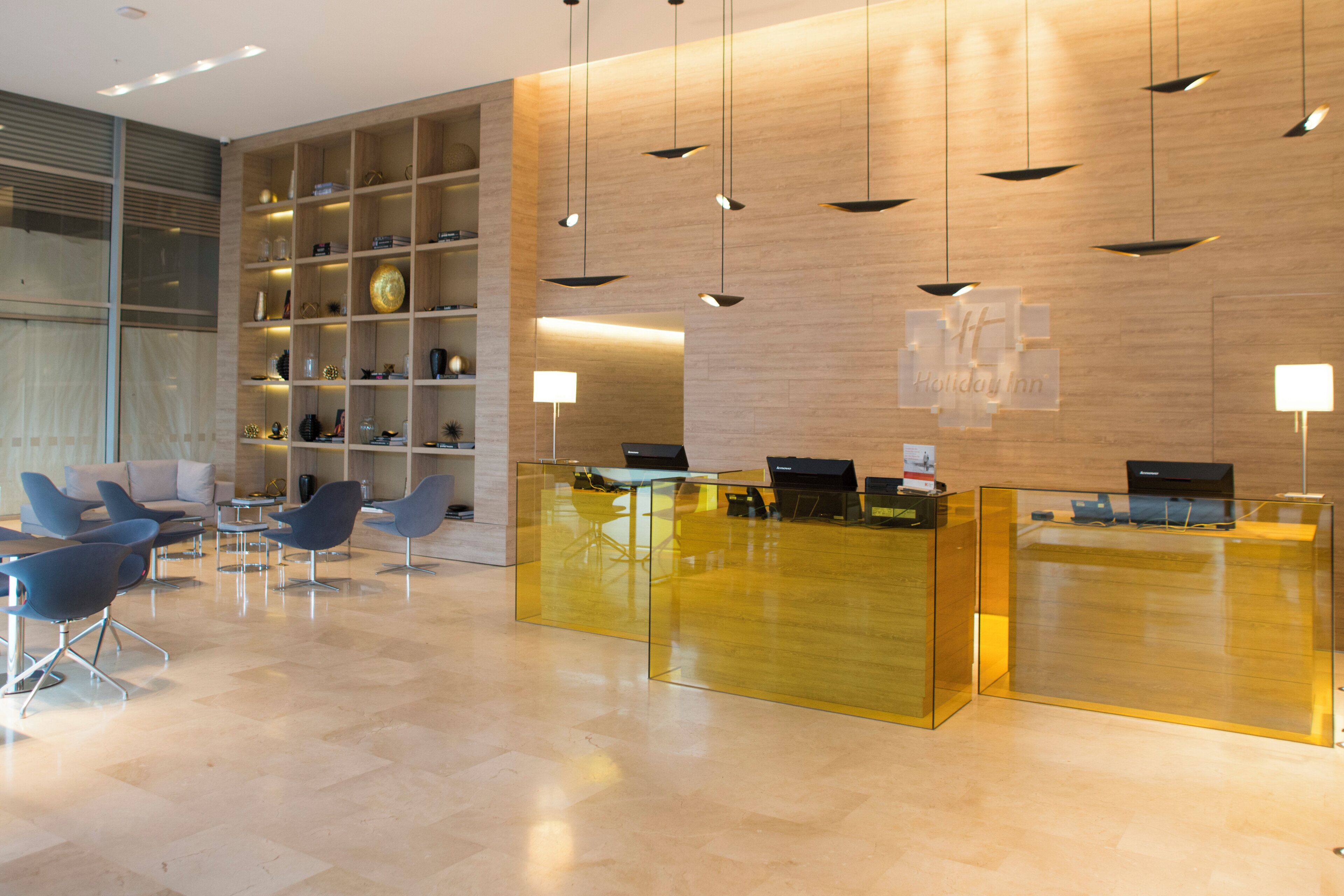 A hotel reception area with a modern design, featuring a reception desk, seating area, and a wall with shelves containing various items.