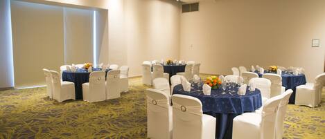 A conference room with round tables, white chairs, and a carpeted floor.