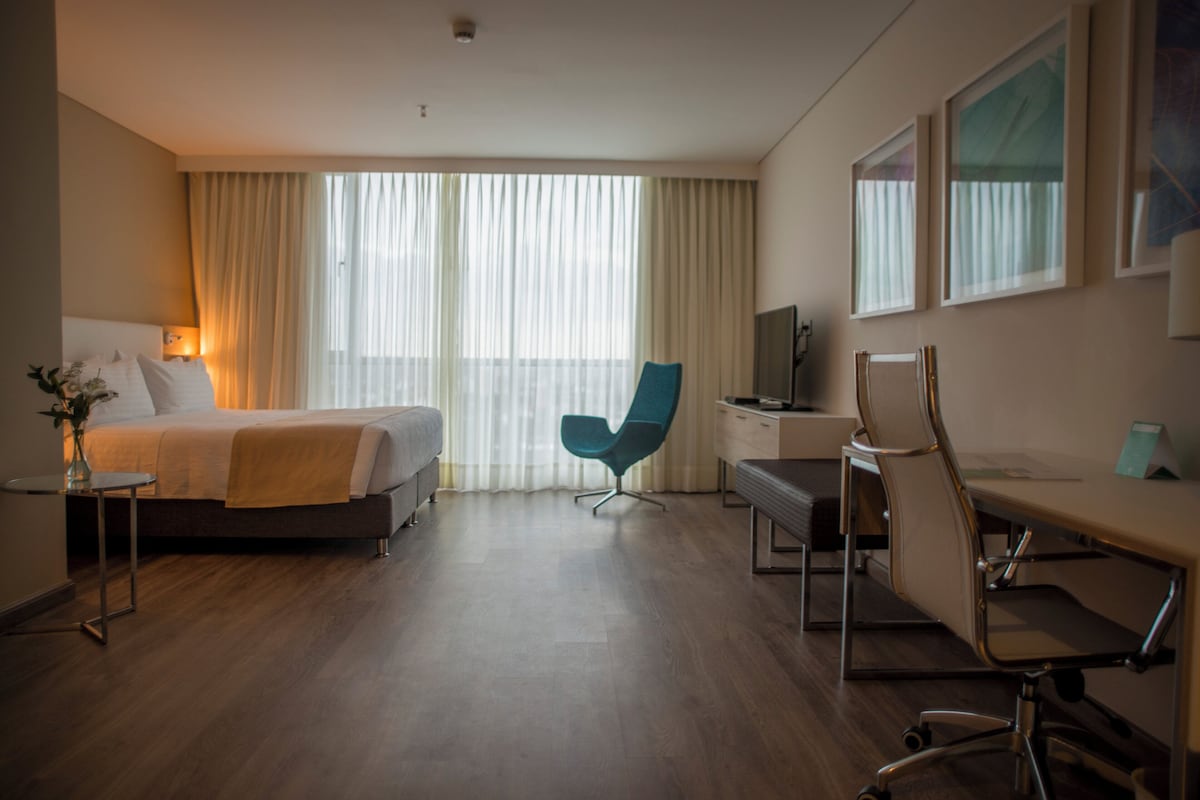 A hotel room with a bed, a desk, a chair, and a television.