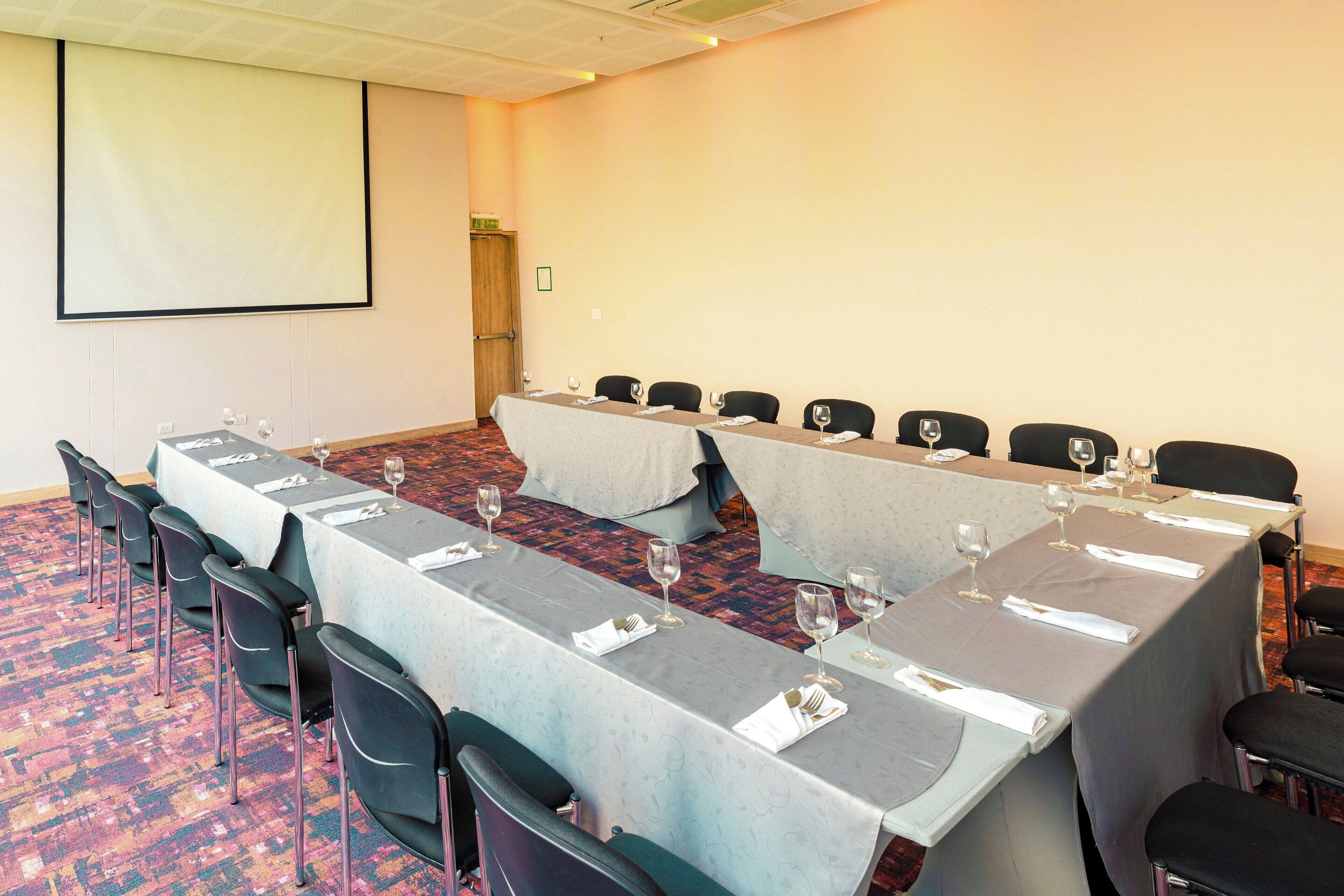 Une salle de conférence avec une longue table préparée pour une réunion, équipée de chaises et de verres à vin.