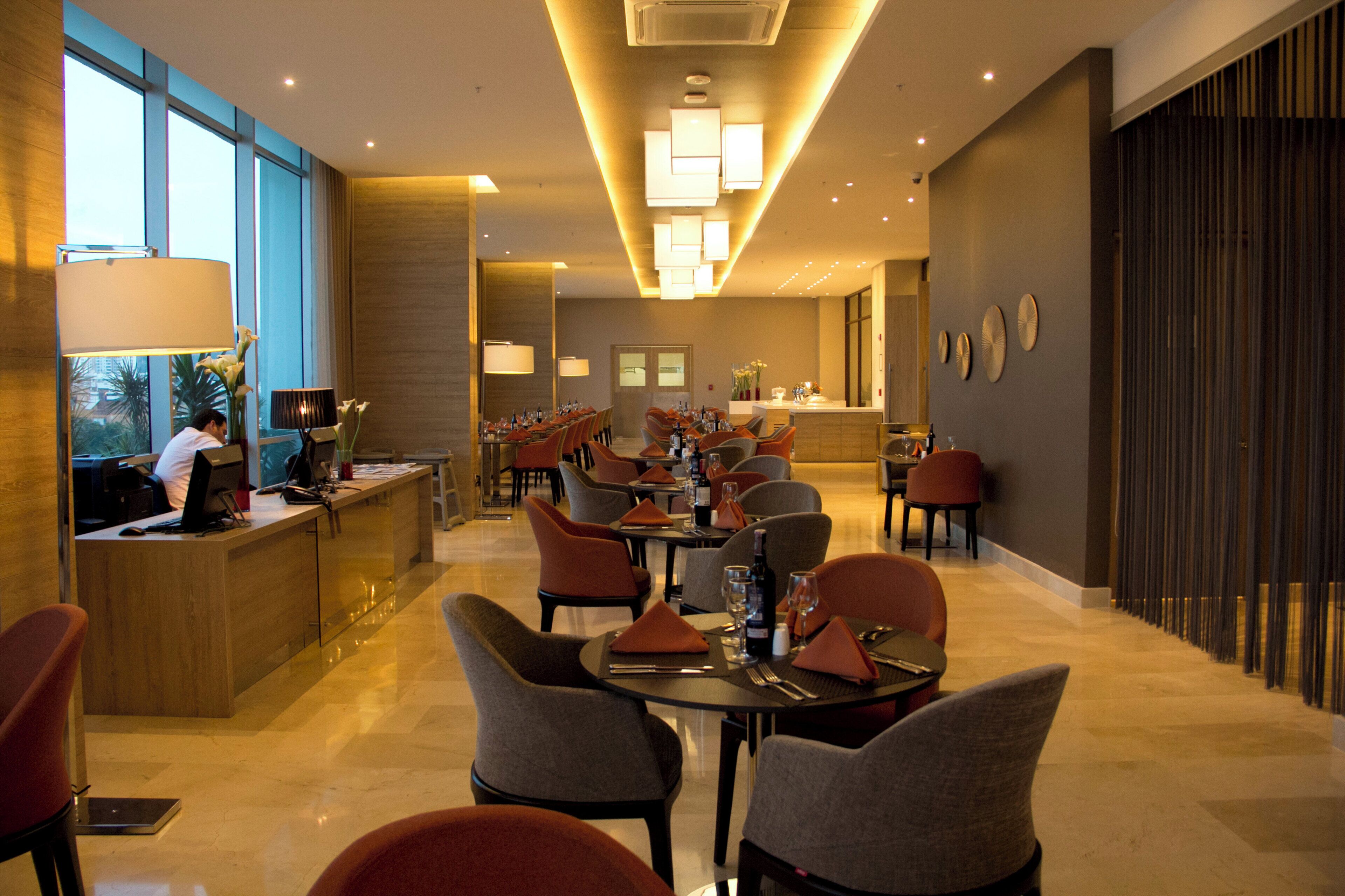 Un vestíbulo de hotel con mostrador de recepción, zona de estar y vistas de la ciudad a través de amplios ventanales.