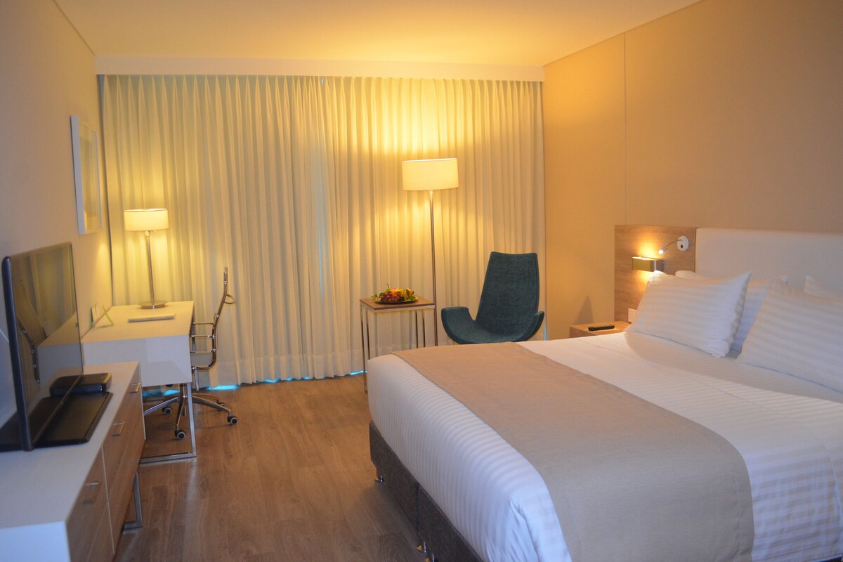 Une chambre d’hôtel avec un lit, un bureau, une chaise et une petite table sur laquelle se trouvent des fruits.
