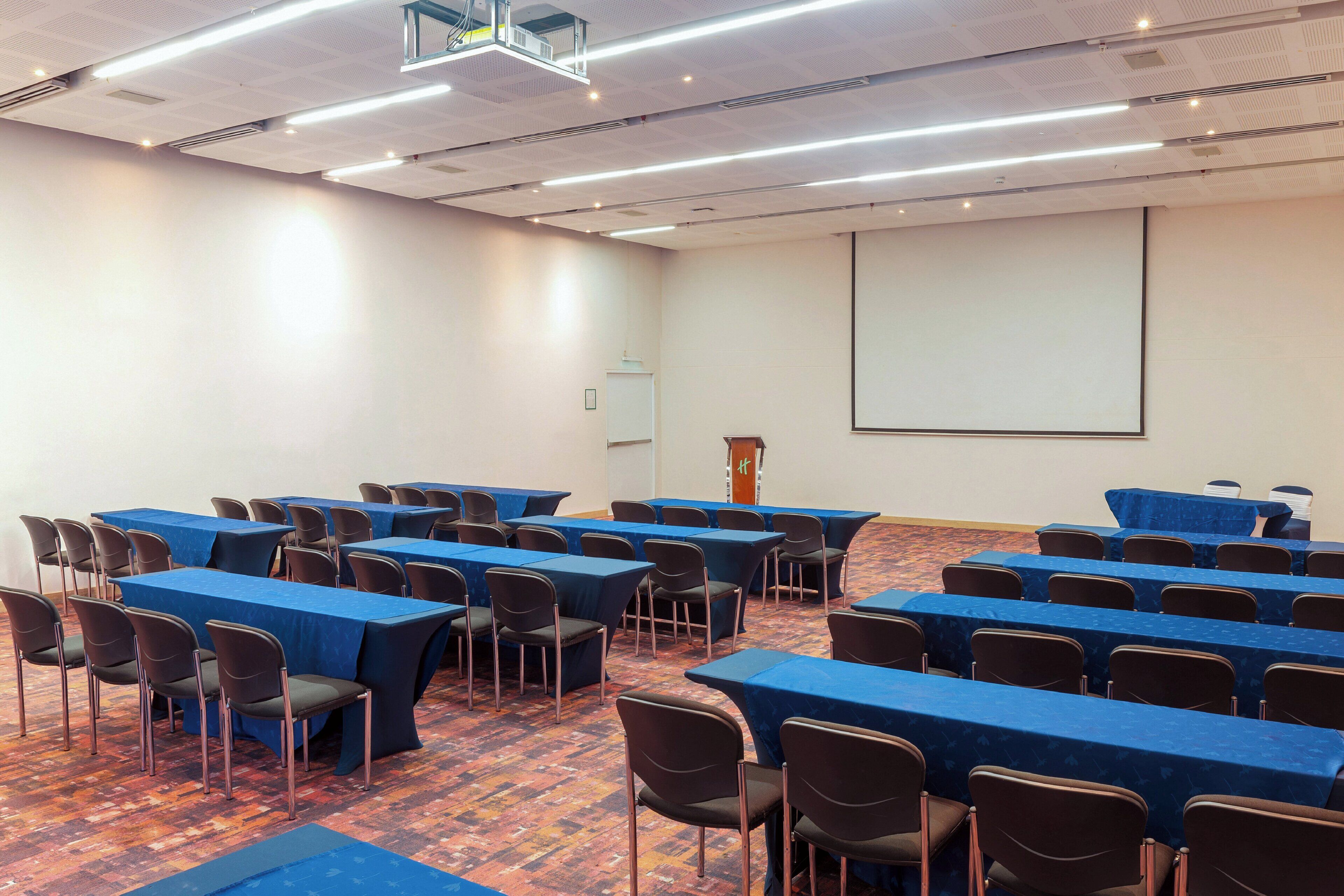 A conference room with rows of tables and chairs, a projector screen, and a whiteboard.