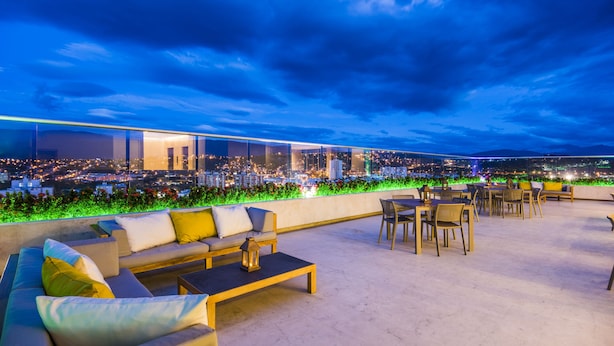 Una terraza en la azotea con mobiliario exterior, vistas a la ciudad y un ambiente bien iluminado.