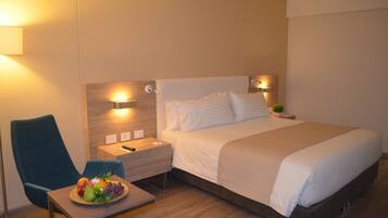 Une chambre d’hôtel avec un lit, des tables de chevet, une chaise et une petite table sur laquelle se trouvent des fruits.