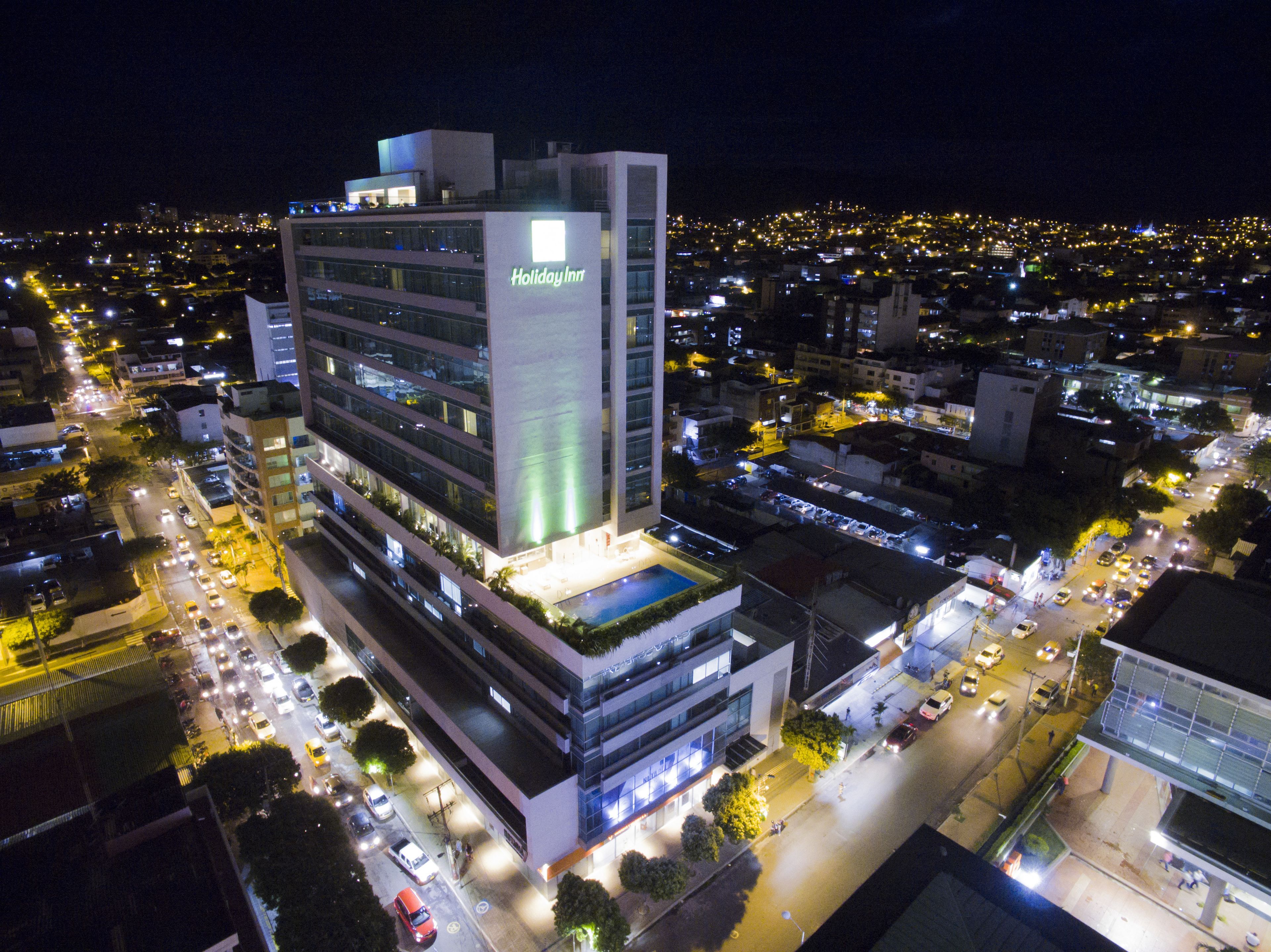 Un hotel Holiday Inn de varios pisos con un letrero llamativo, rodeado de una concurrida zona urbana por la noche.