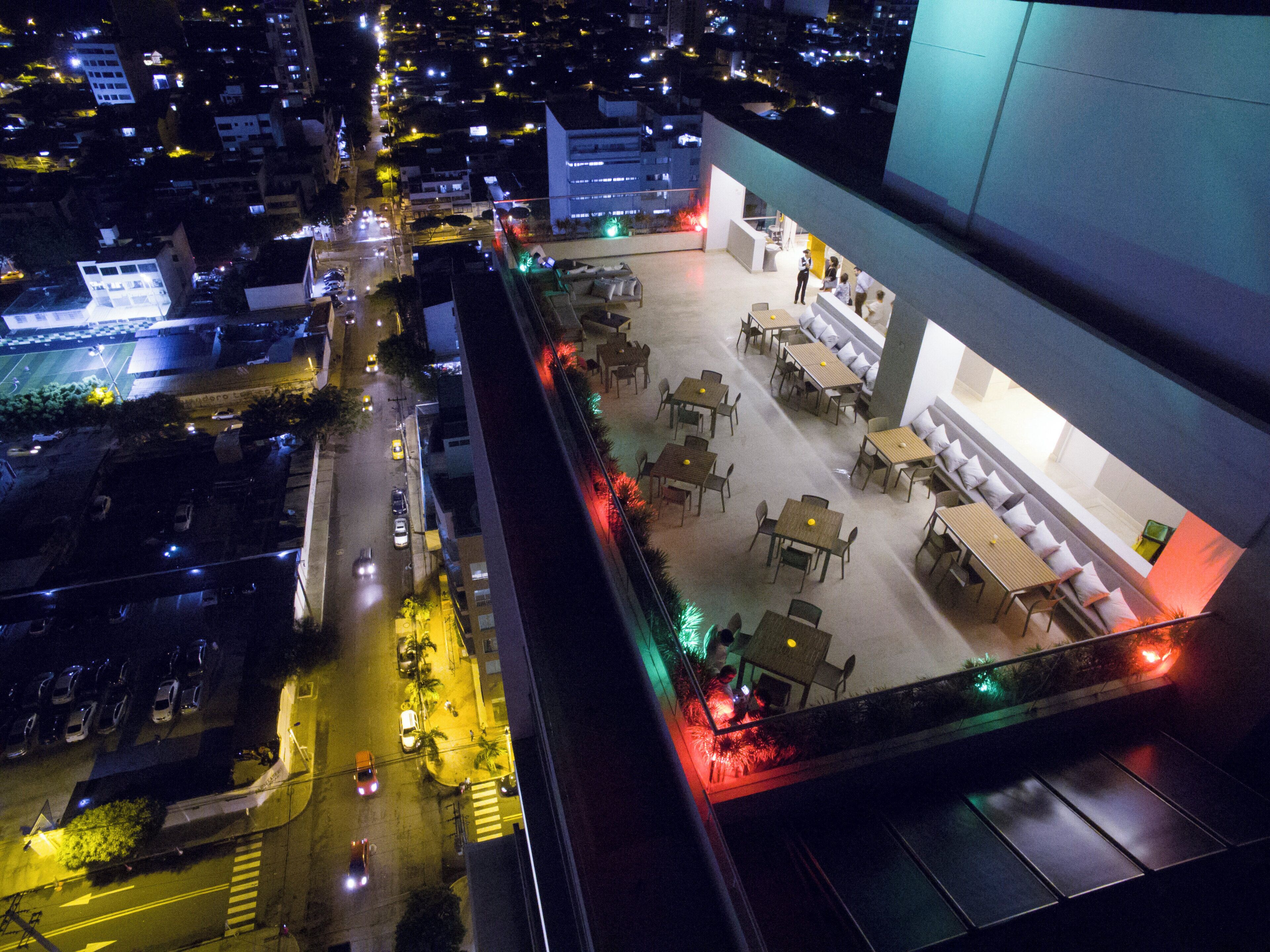 A rooftop terrace with tables and chairs, a view of the cityscape, and a building with a modern design.