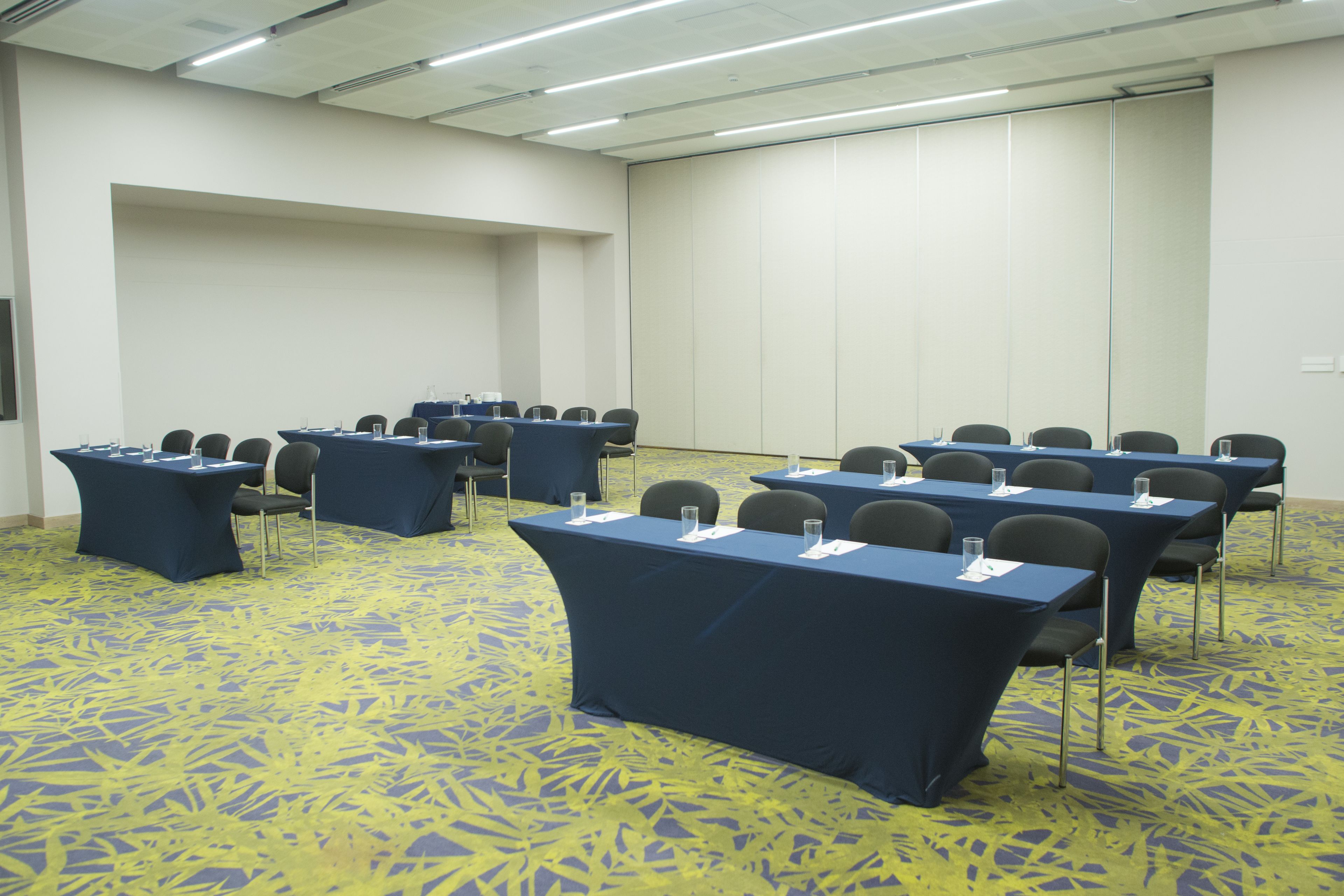 A conference room with tables and chairs, carpeted floor, and a large whiteboard wall.