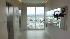 Habitación de hotel moderna con un ventanal que ofrece vistas a la ciudad, un estante empotrado con toallas y un cartel en la pared.