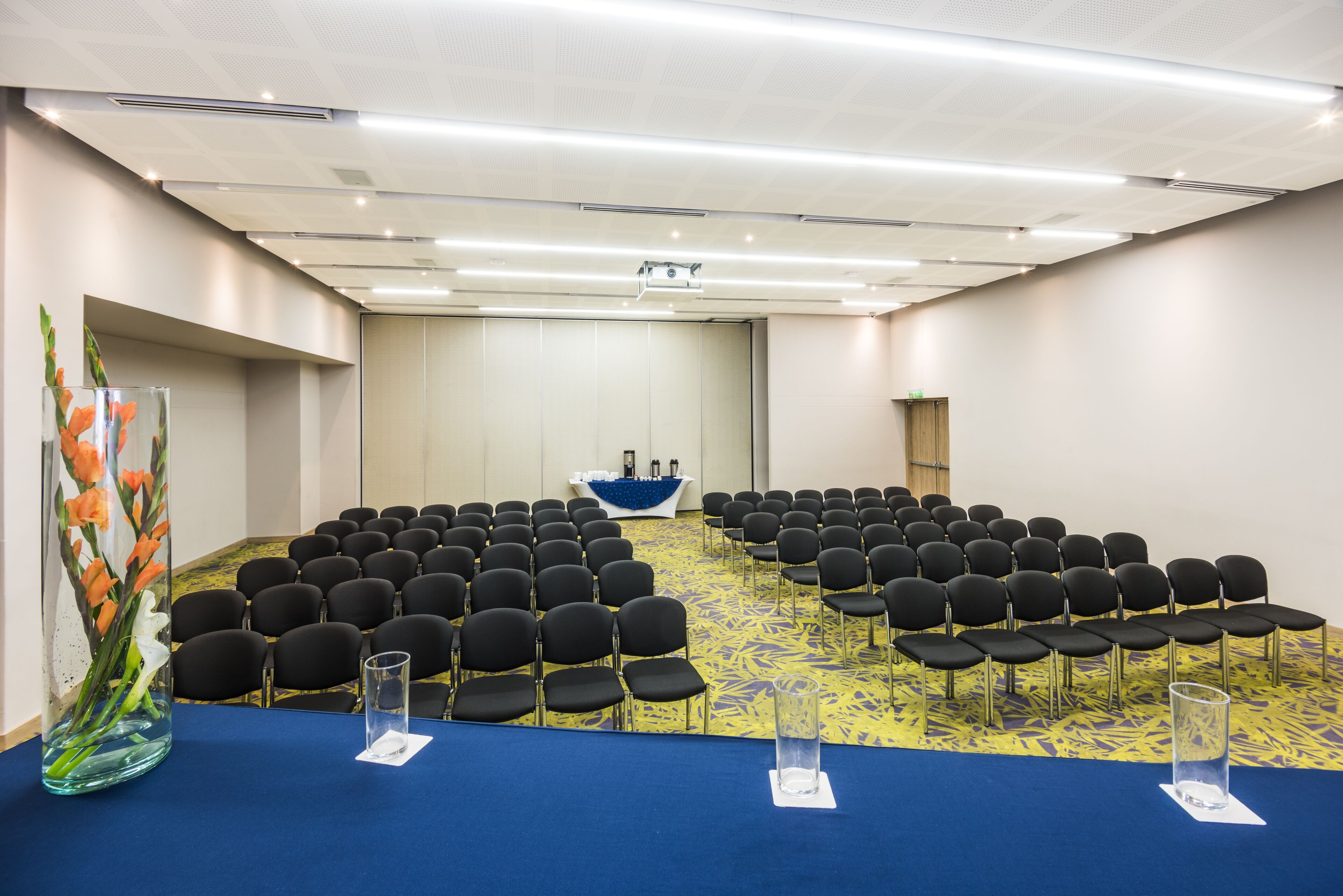 A conference room with rows of chairs, a podium, and a large vase with flowers.
