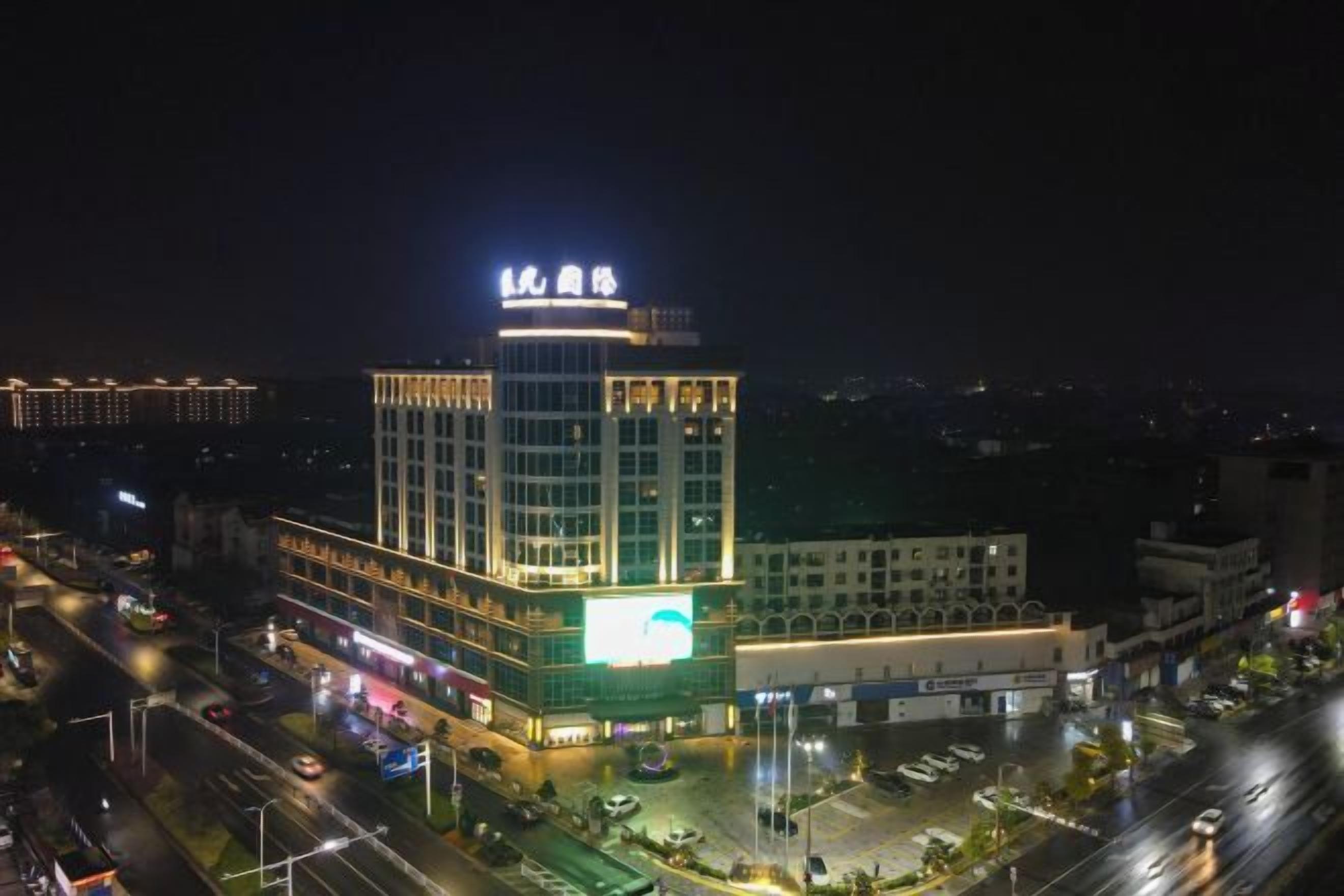 Un hotel de varios pisos con un letrero llamativo en la parte superior, una zona de estacionamiento al frente y una fachada bien iluminada.