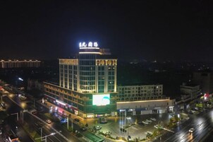 Un hotel de varios pisos con un letrero llamativo en la parte superior, una zona de estacionamiento al frente y una fachada bien iluminada.
