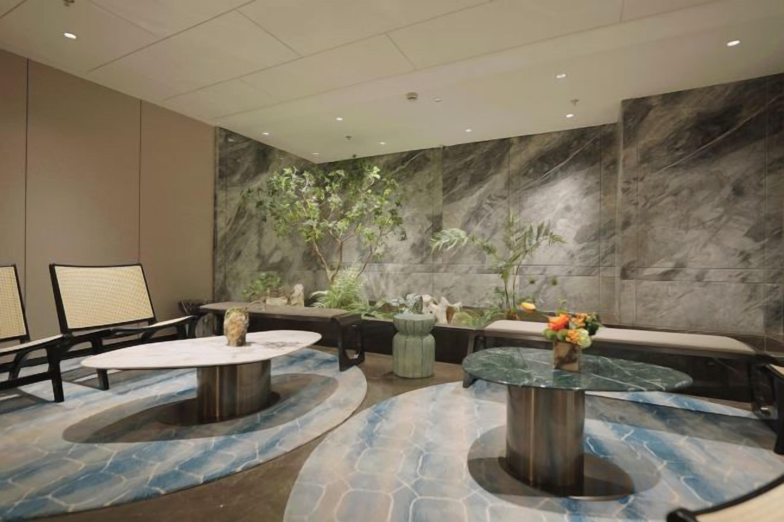 A lobby with marble walls, seating areas, and a central plant arrangement.