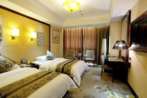 A hotel room with two beds, a desk, a chair, and a lamp.