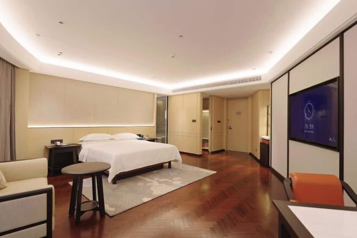 Una habitación de hotel moderna con una cama grande, una zona de estar con una pequeña mesa y un televisor montado en la pared.
