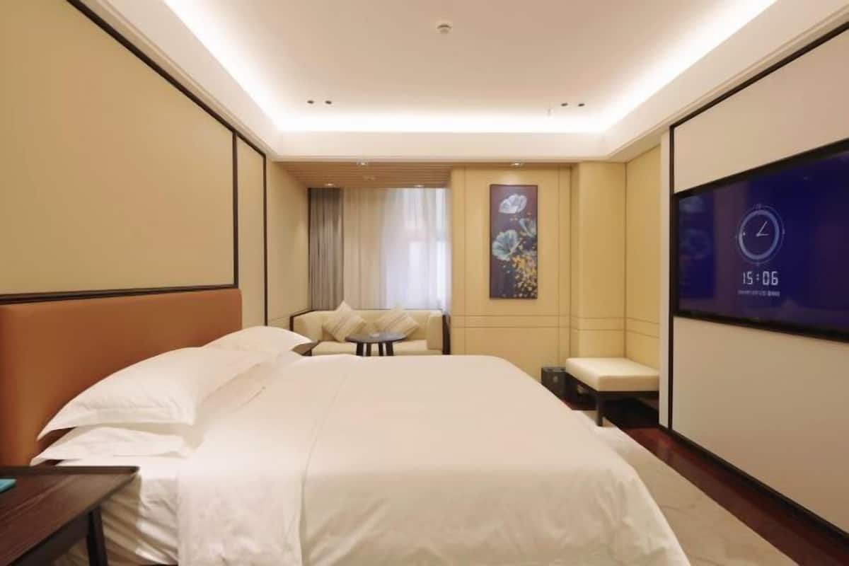 Una habitación de hotel con una cama grande, una zona de estar, un televisor y un reloj en la pared.