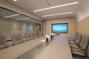 Un salón de conferencias con una mesa larga, sillas, una pantalla grande y un separador de vidrio.