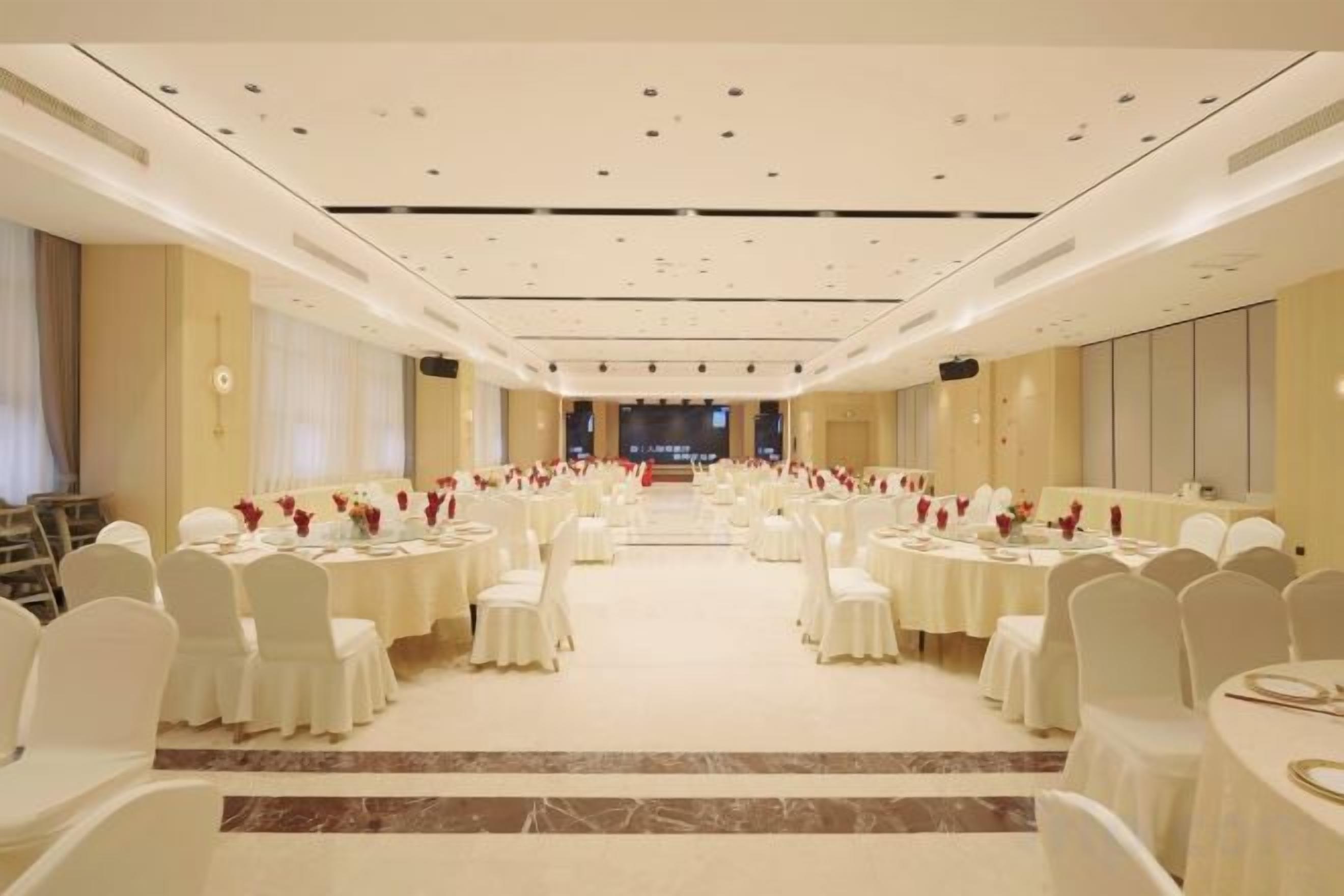Un salón de banquetes con mesas redondas, sillas blancas y un escenario central.