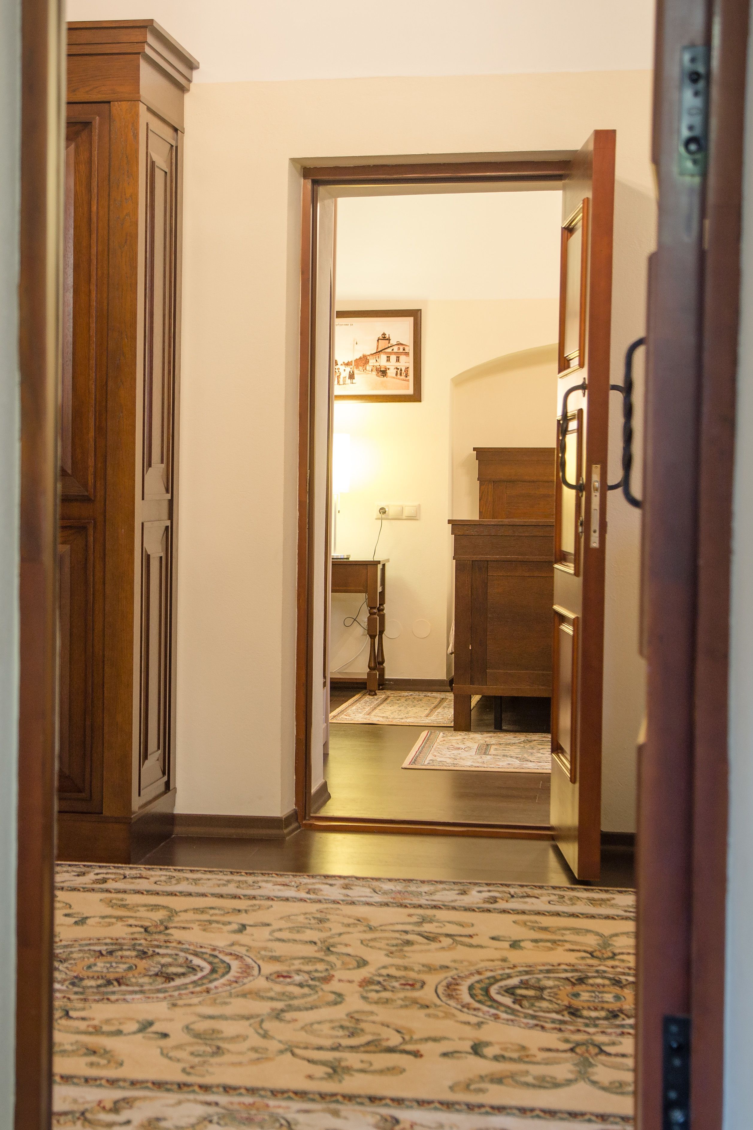 A hallway with a wooden cabinet, a rug, and a desk with a lamp.