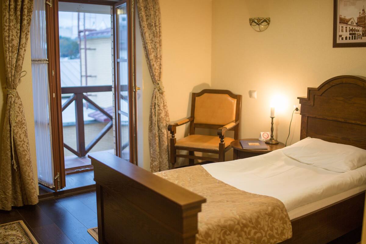 A hotel room with a wooden bed, a chair, a nightstand with a lamp, and a view through a glass door.