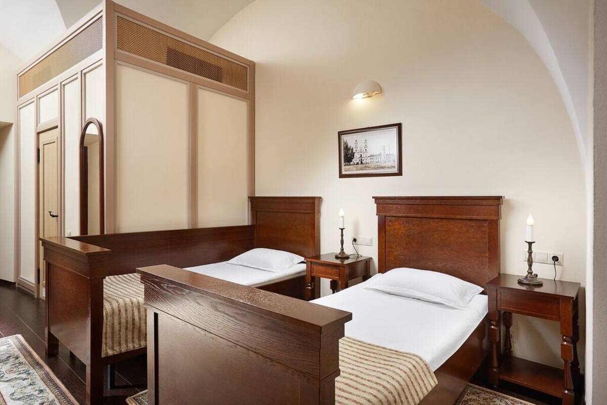 A traditional bedroom with two single beds, a wooden wardrobe, and a framed picture on the wall.