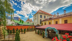 A courtyard with a red-roofed building, a green-roofed building, and a white building with a red roof. There are potted plants and a flower bed with red flowers. - Hotel Monastyrski Minsk City Centre (Minsk)