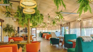 A spacious indoor area with wooden flooring, green and orange seating, and hanging plants. - Hotel Monastyrski Minsk City Centre (Minsk)