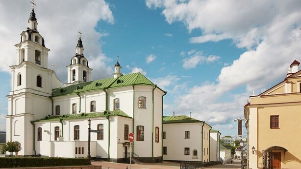A white church with a green roof and two towers, surrounded by a paved area and a chain-link fence. - Hotel Monastyrski Minsk City Centre (Minsk)