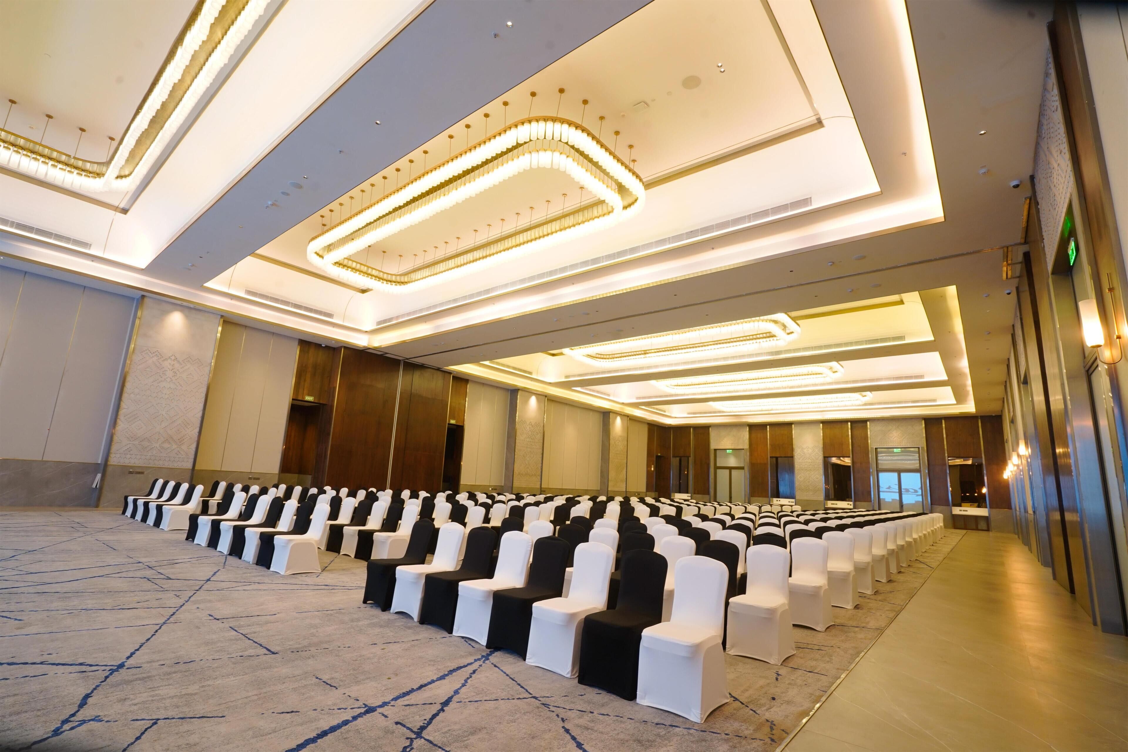 Un salón de conferencias con hileras de sillas, piso alfombrado e iluminación moderna.
