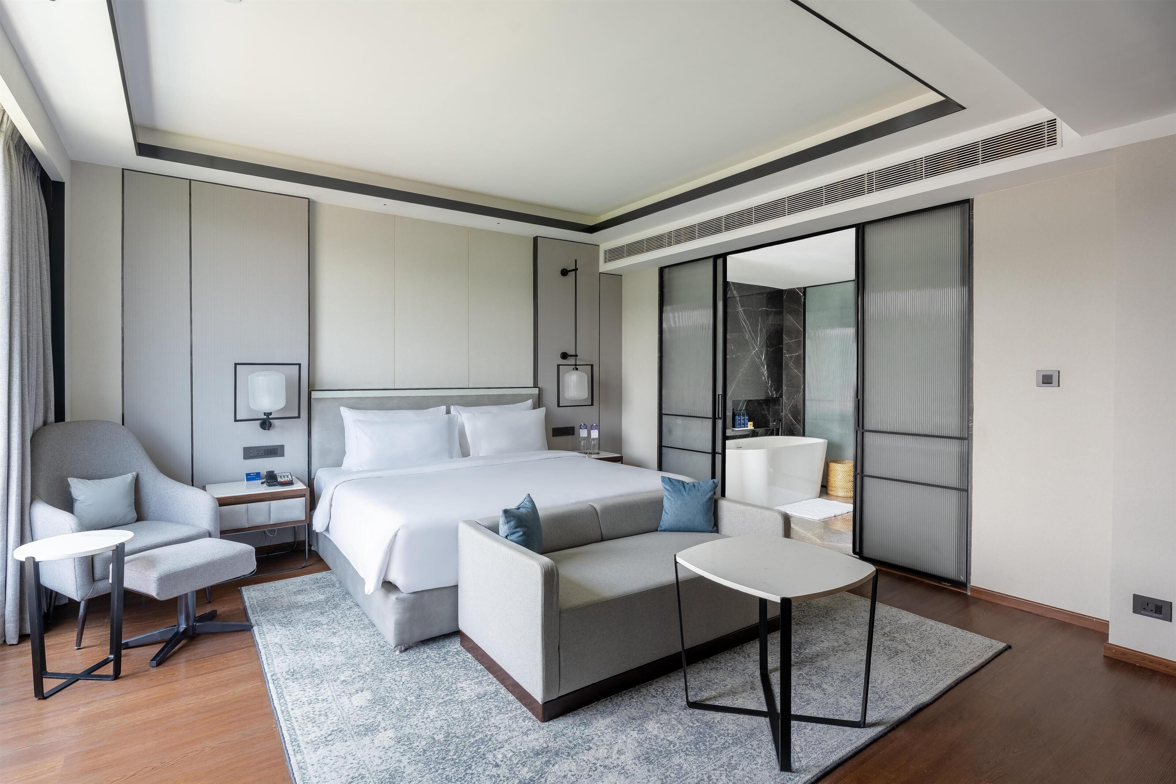 Una habitación de hotel moderna con una cama grande, un sofá, una mesita y una silla.