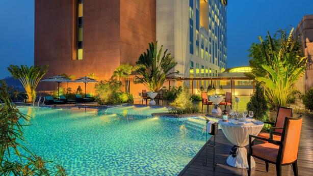 Un espace piscine d’hôtel comprenant une piscine carrelée, des chaises longues et des parasols.