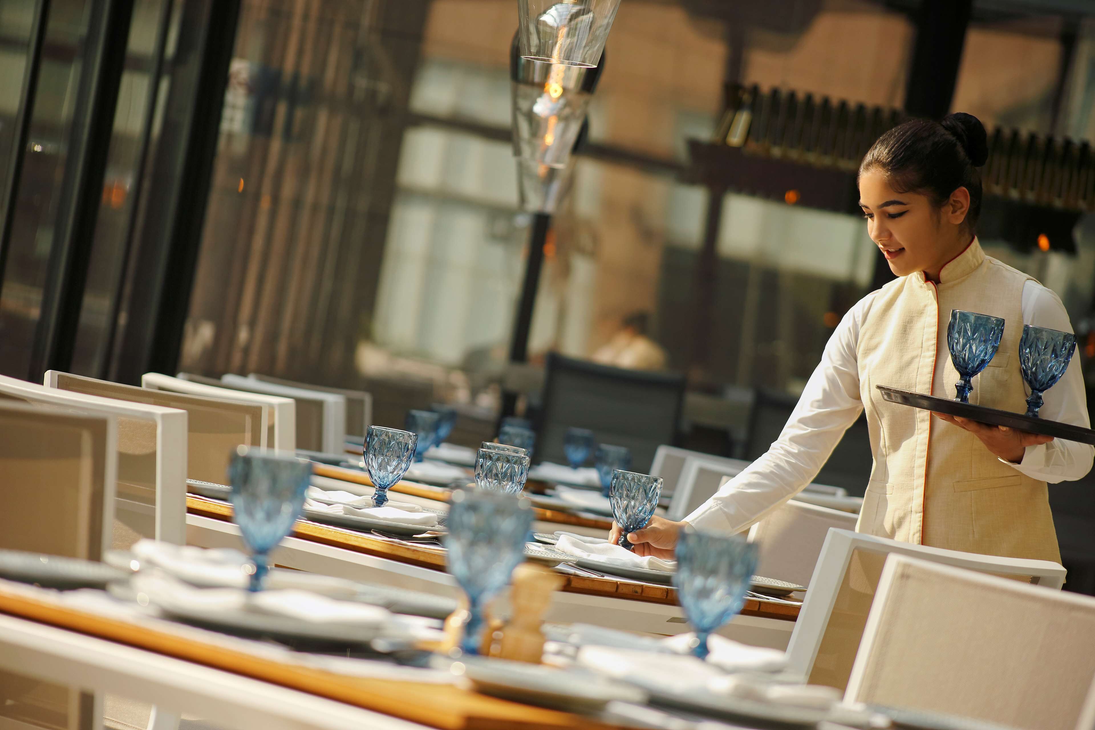 A restaurant setting with neatly arranged tables, each with a blue glass and a white plate.