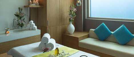 A modern spa room with a bed, a tea set, and towels.