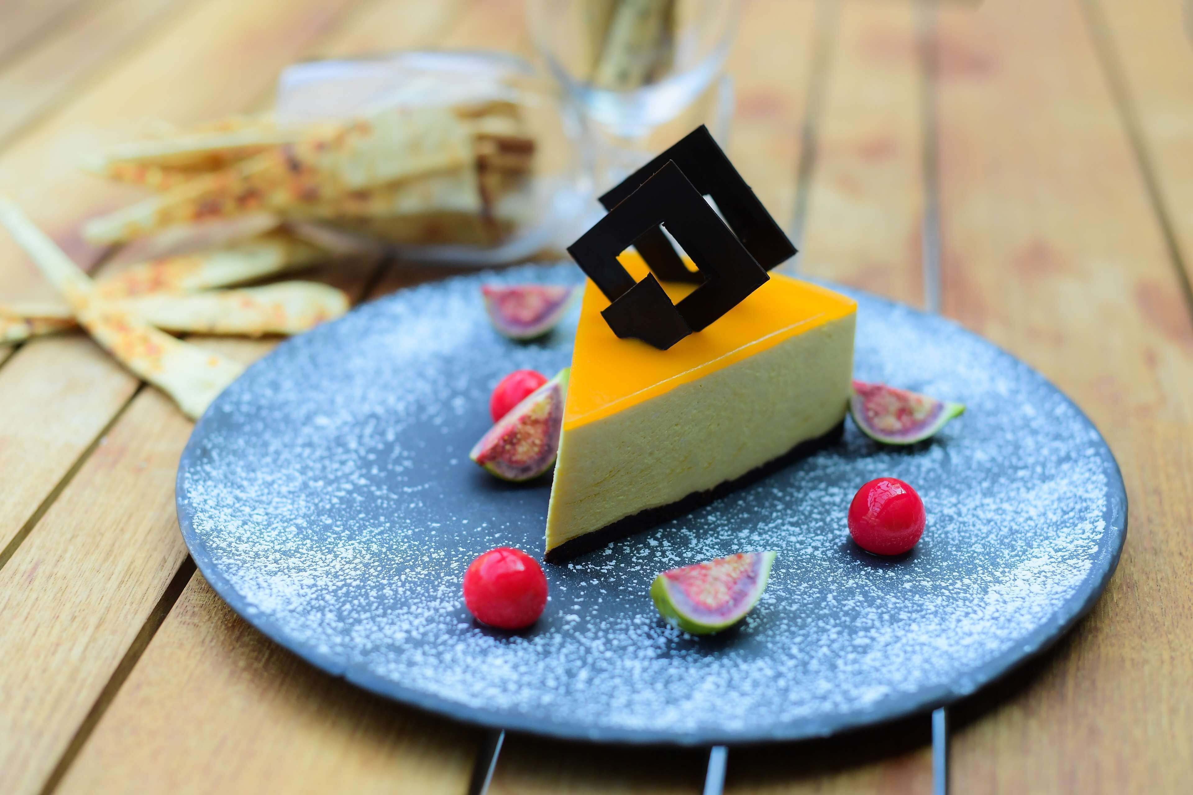 A dessert plate with a slice of cheesecake, figs, and red berries on a textured blue plate.