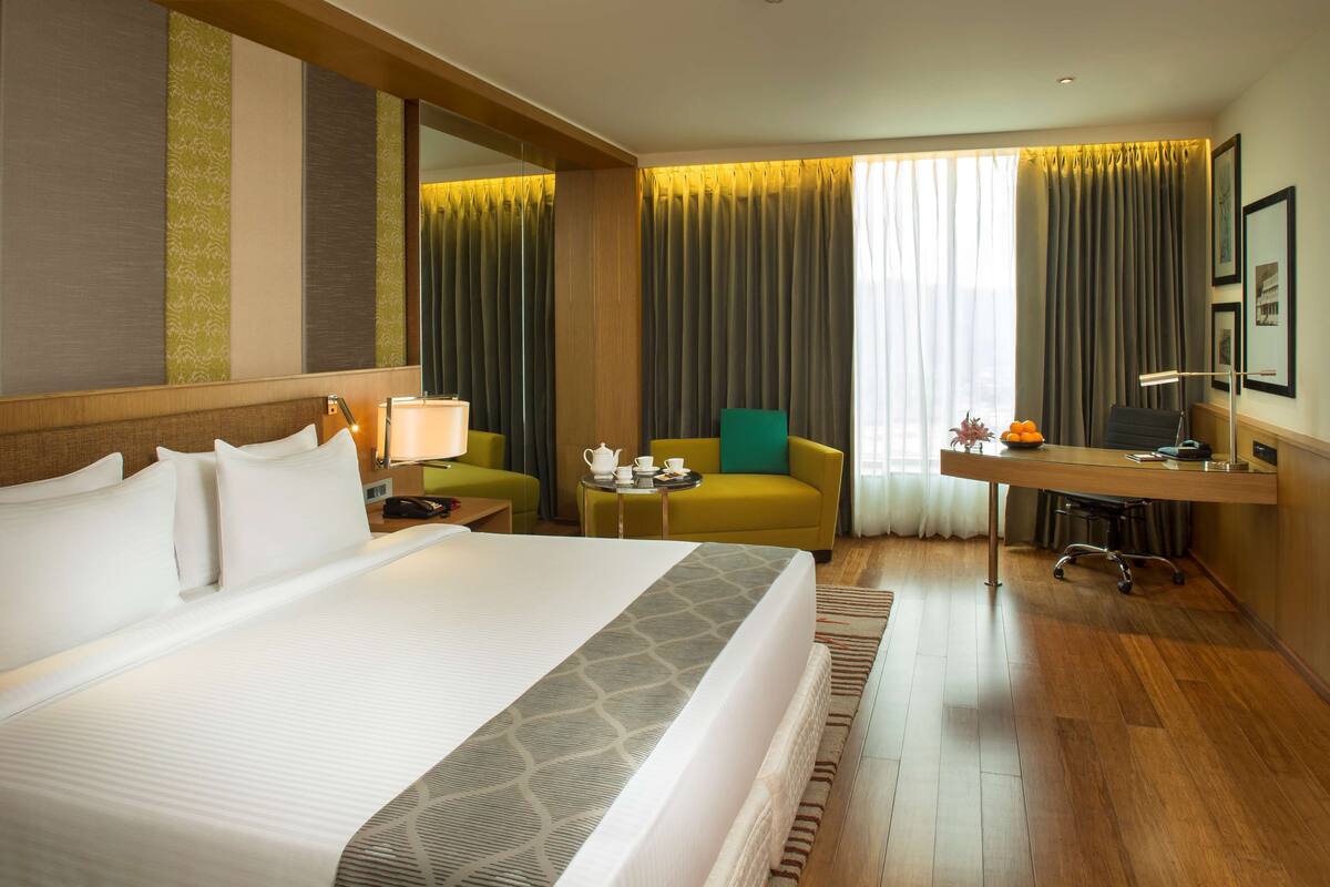 Ein Hotelzimmer mit einem großen Bett, einem Schreibtisch mit Stuhl, einem kleinen Tisch mit Lampe und einer Couch.