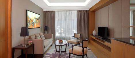 Una habitación de hotel moderna con sofá, dos sillones, una mesa de centro, televisor y un cuadro en la pared.