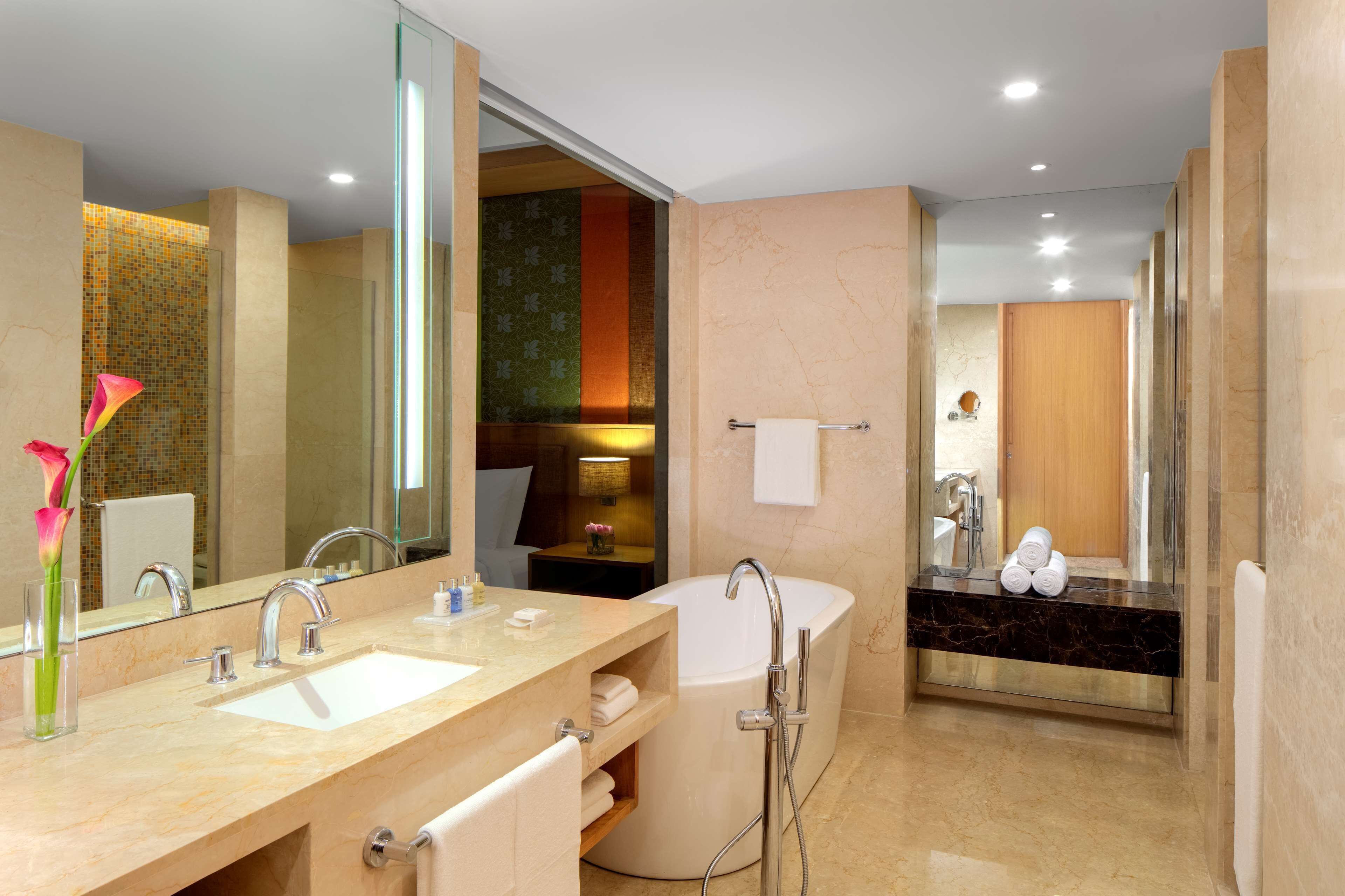A modern bathroom with a double sink vanity, a large mirror, a freestanding bathtub, and a towel rack.
